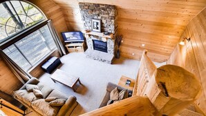 Interior acogedor de una cabaña con chimenea de piedra, paredes de madera, un sofá y una televisión.