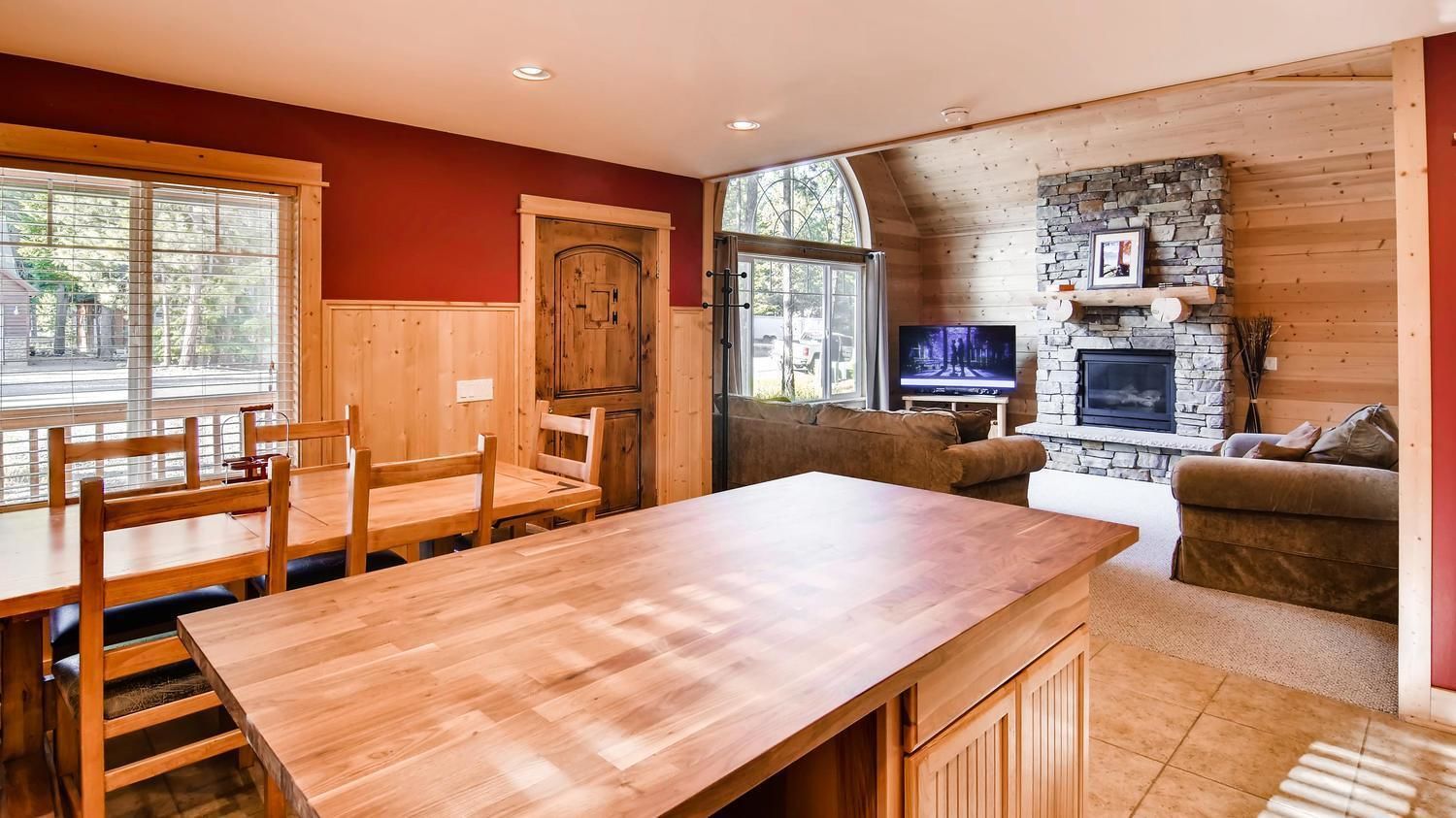A cozy living room with a wooden dining table, a stone fireplace, and a television.