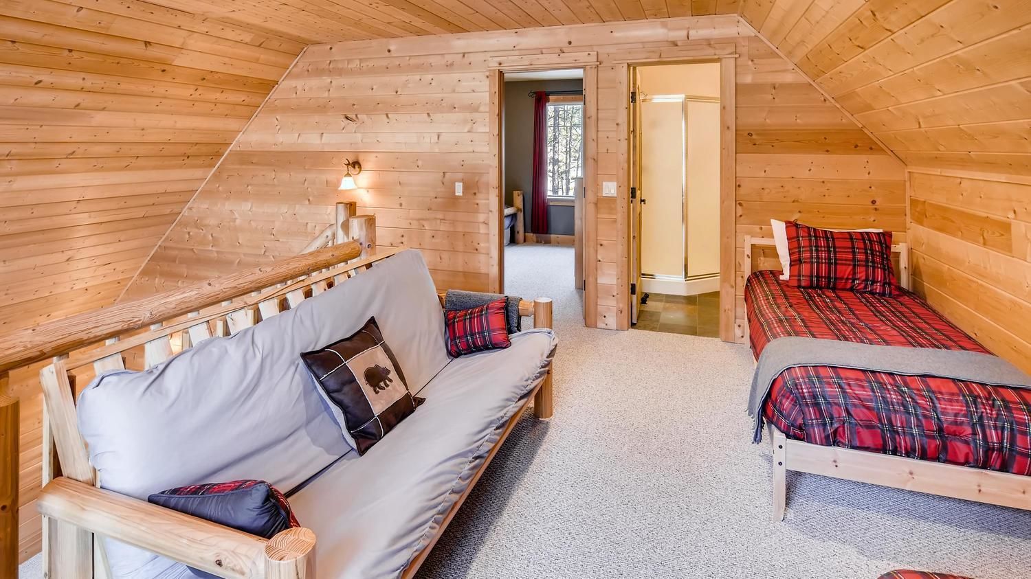 A cozy attic bedroom with a wooden sloped ceiling, a sofa, a bed, and a small table.