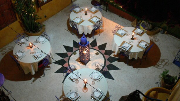 Un comedor con mesas redondas, cada una dispuesta con platos, cubiertos y velas.