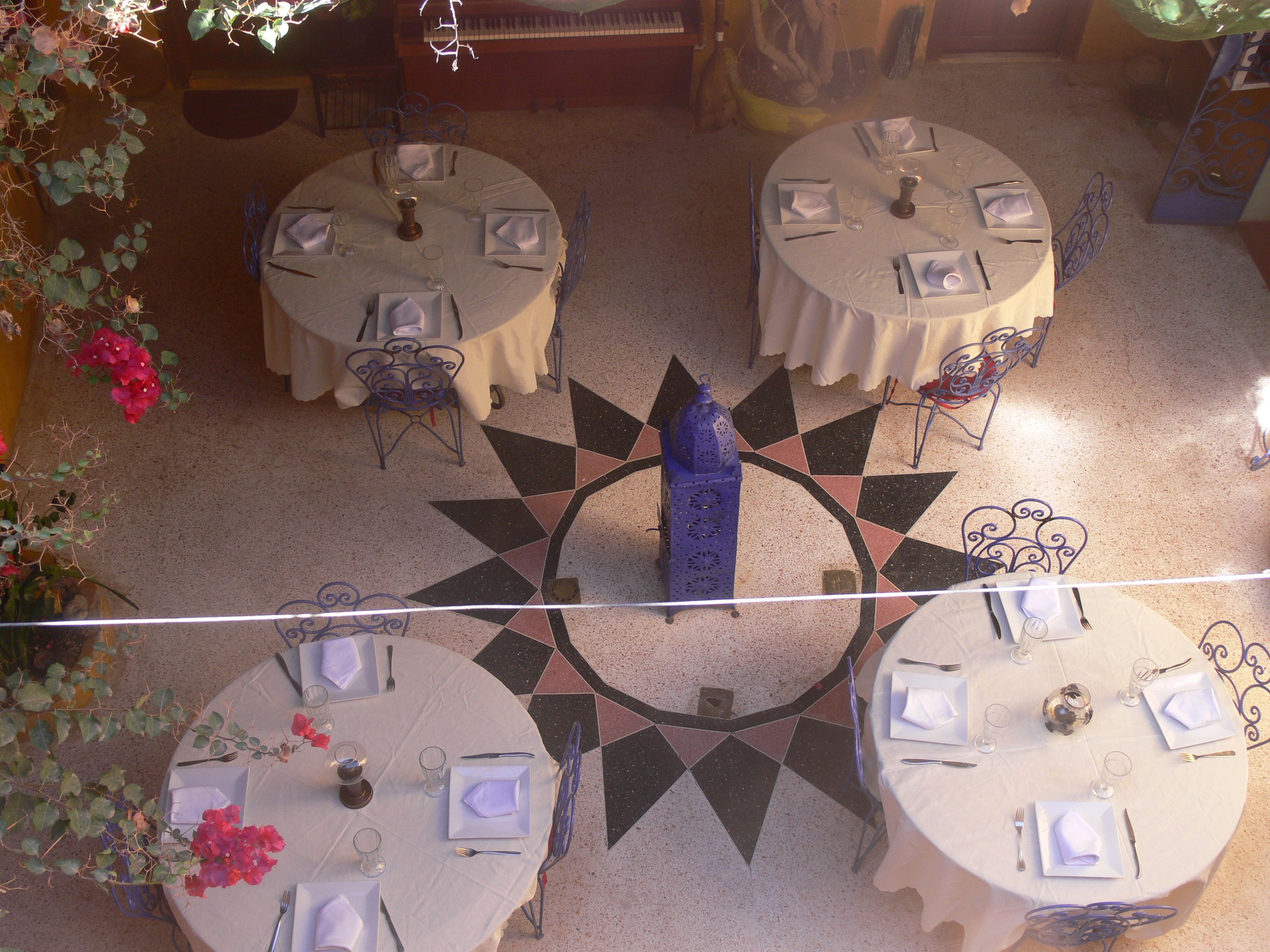 Un comedor con mesas redondas dispuestas para cuatro comensales, cada una con mantel blanco, servilletas, cubiertos y vasos.