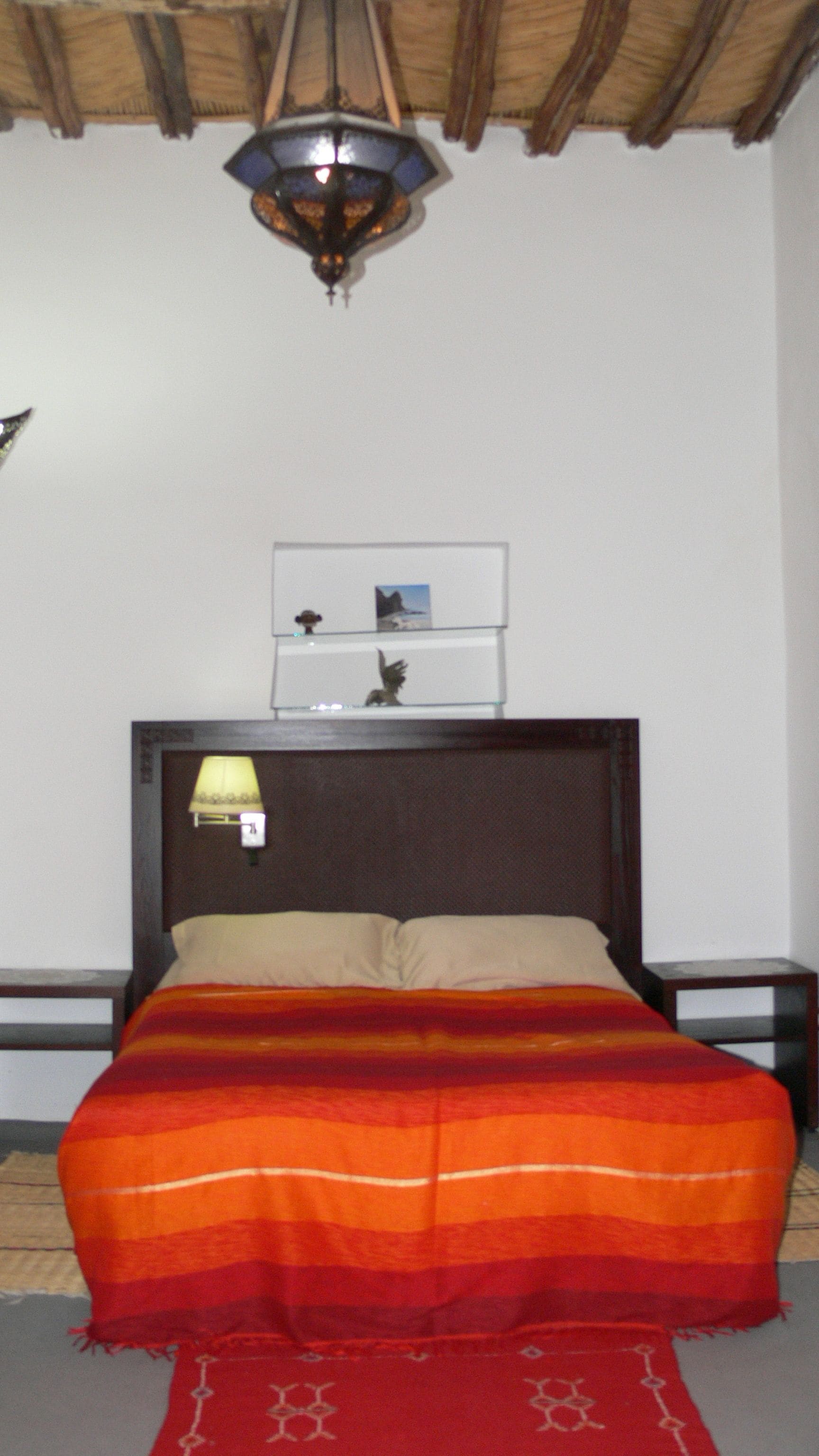 A bed with a striped blanket, a nightstand with a lamp, and a shelf with a picture and a small statue.