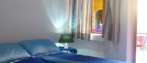A bedroom with a bed, two framed pictures on the wall, a window with curtains, and a nightstand with a lamp.