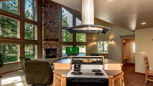 A spacious kitchen with a stone fireplace, large windows, and a modern stove. - Tall Pines (Cle Elum)