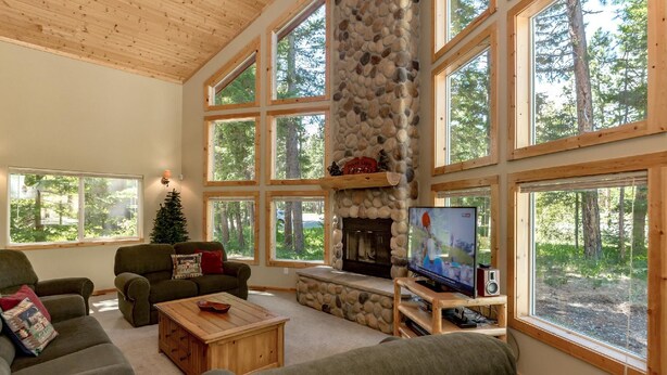 A spacious living room with large windows, a stone fireplace, and a cozy seating area. - Tall Pines (Cle Elum)