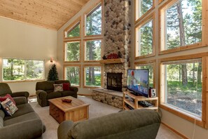 A spacious living room with large windows, a stone fireplace, and a cozy seating area. - Tall Pines (Cle Elum)