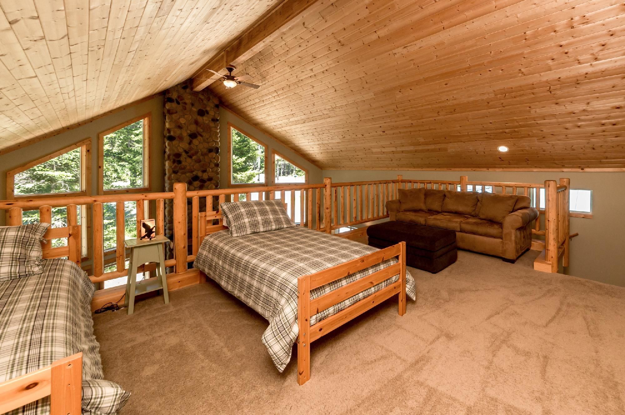 A cozy cabin with a loft bedroom featuring a bed, a sofa, and a wooden railing.