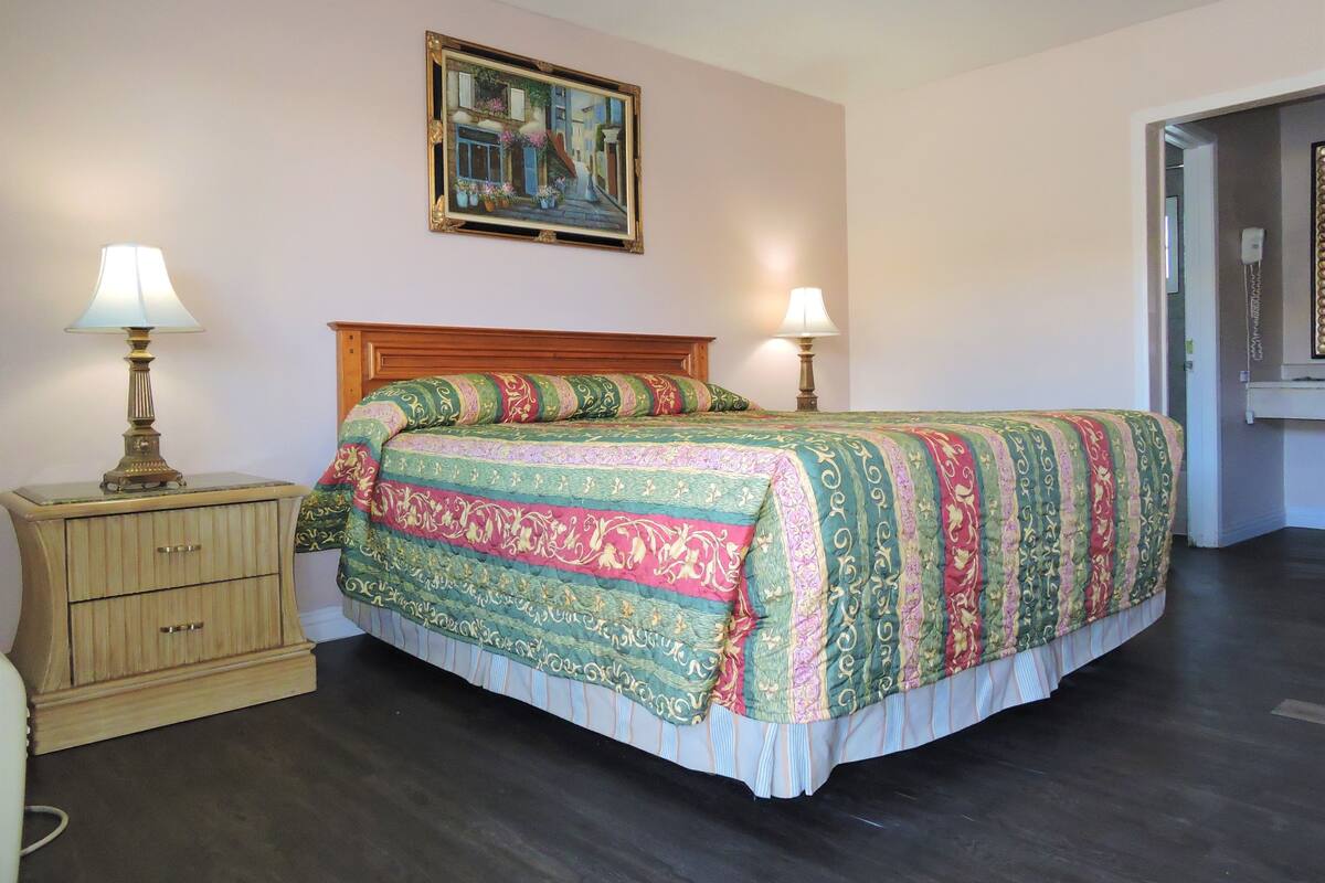 A bedroom with a wooden bed, two bedside lamps, a nightstand, and a painting on the wall.