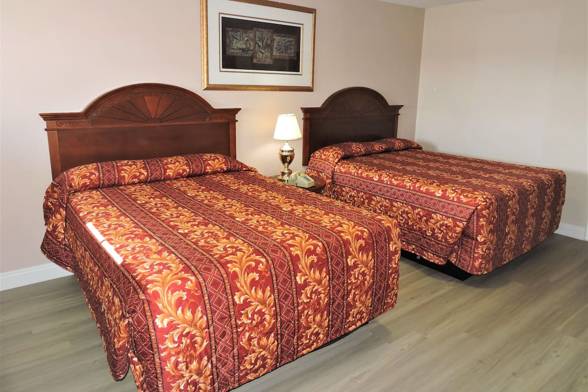 A hotel room with two beds, a wooden headboard, a framed picture on the wall, and a bedside lamp.