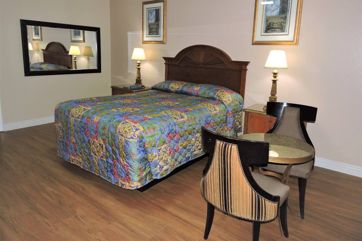 A hotel room with a large bed, two bedside lamps, a chair, and a desk.