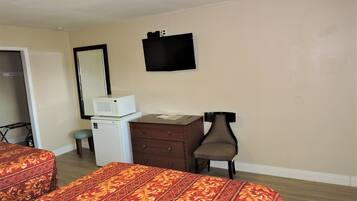 A hotel room with two beds, a dresser, a microwave, a chair, and a television on the wall.