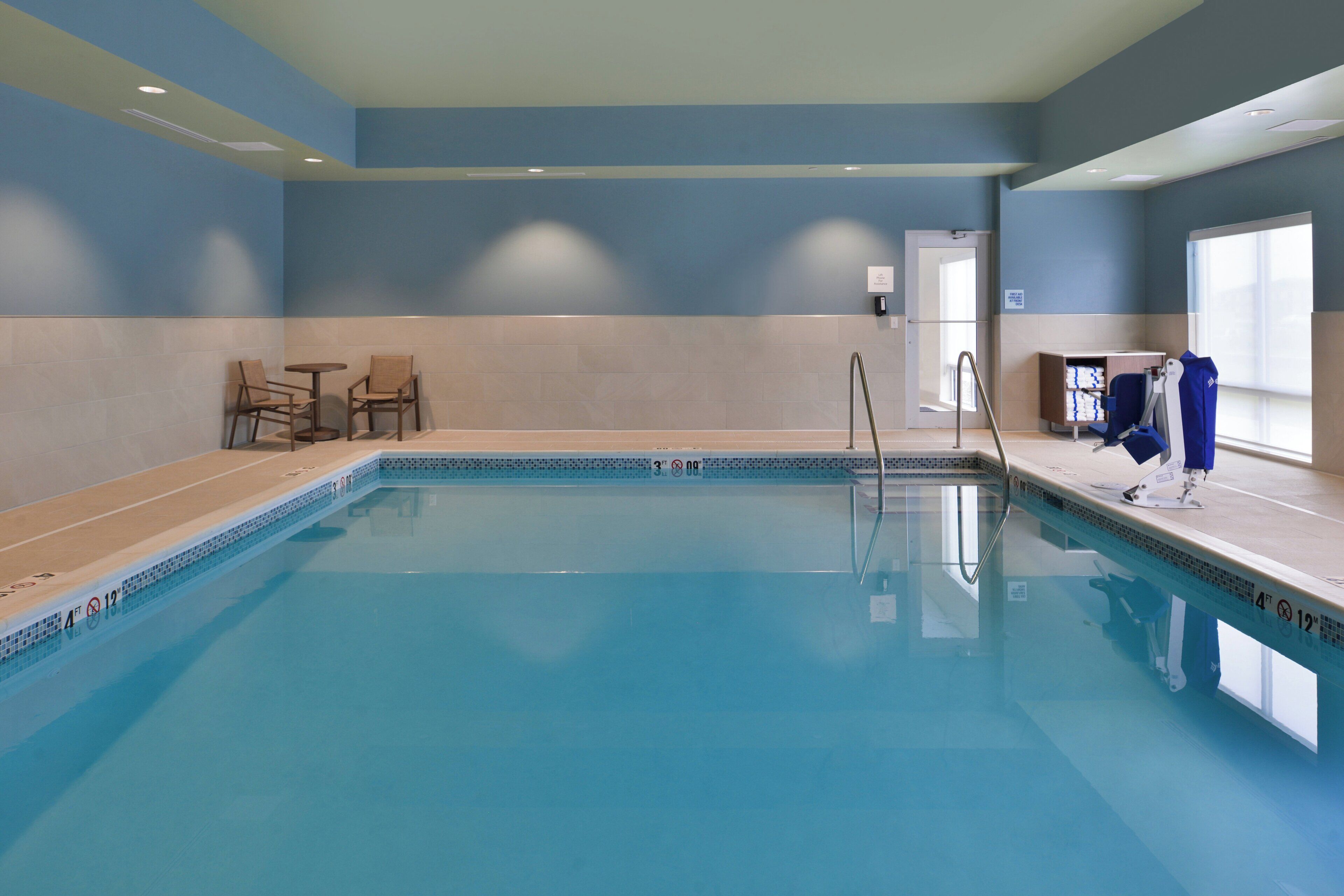Une piscine à l’eau d’un bleu limpide, avec un plongeoir et un espace détente équipé de chaises.