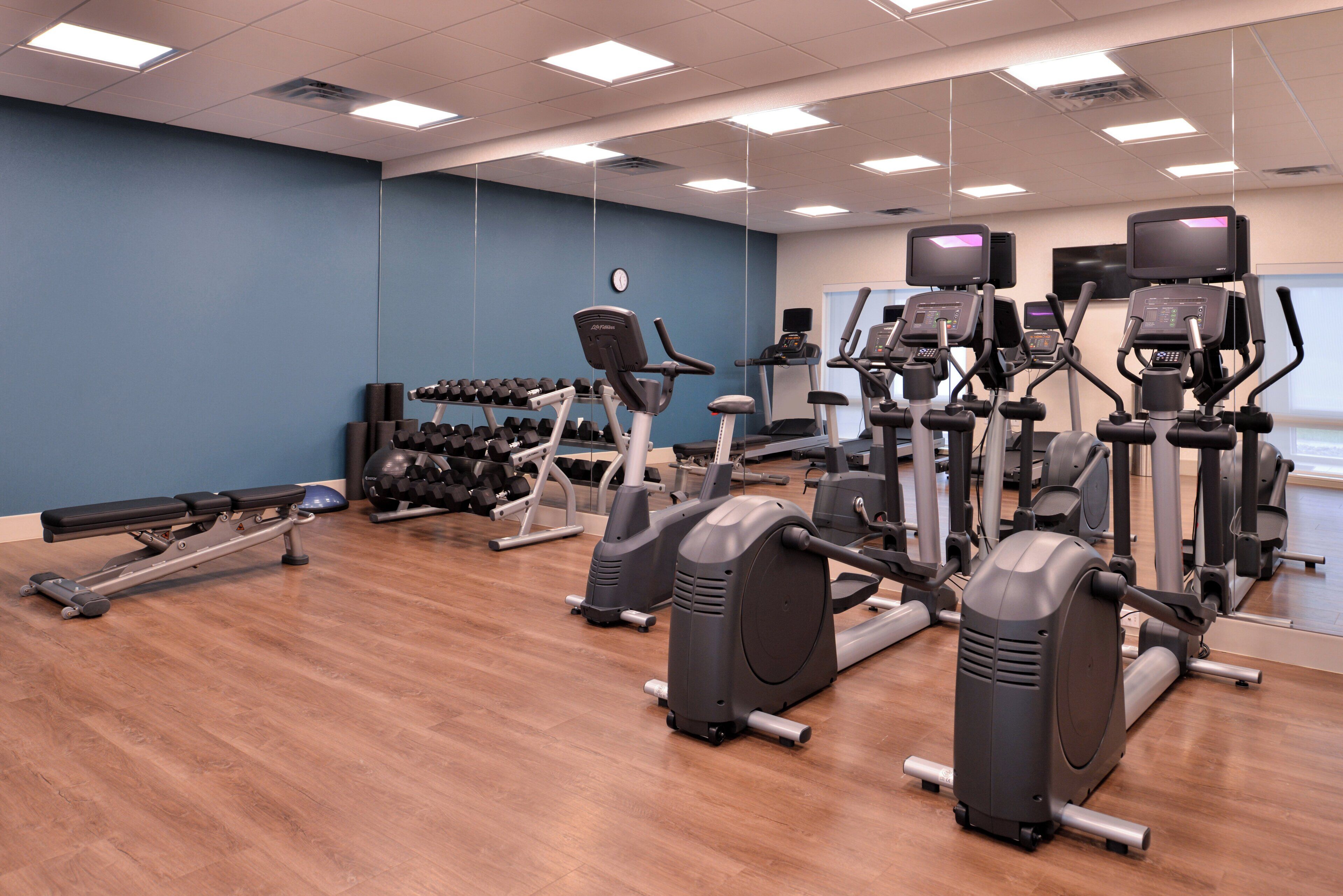 A gym with various exercise equipment, including treadmills, elliptical machines, and dumbbells.