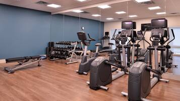 Une salle de sport équipée de divers appareils d’exercice, notamment des tapis de course, des appareils elliptiques et des haltères.