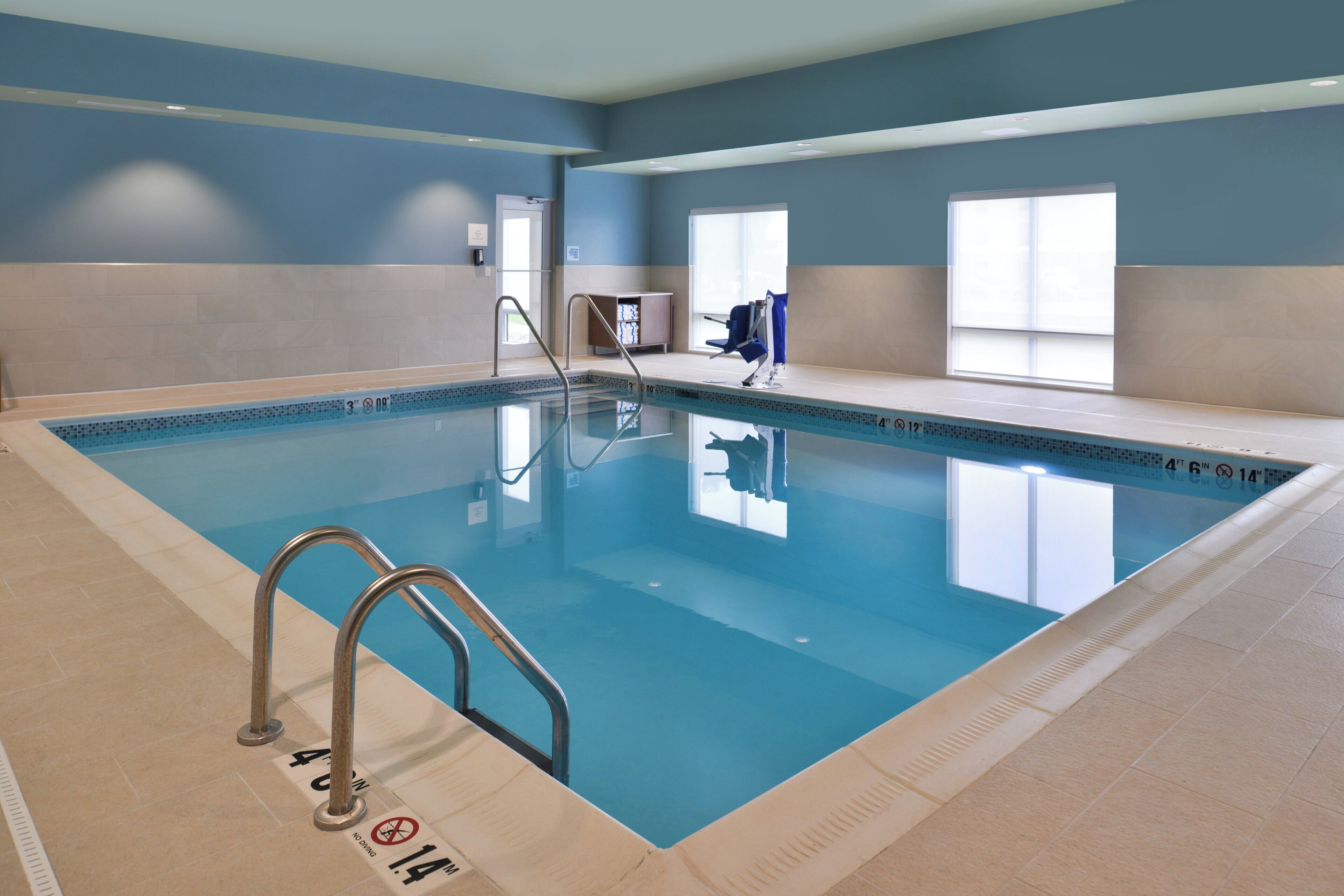 An indoor swimming pool with clear water, a diving board, and a lifeguard chair.