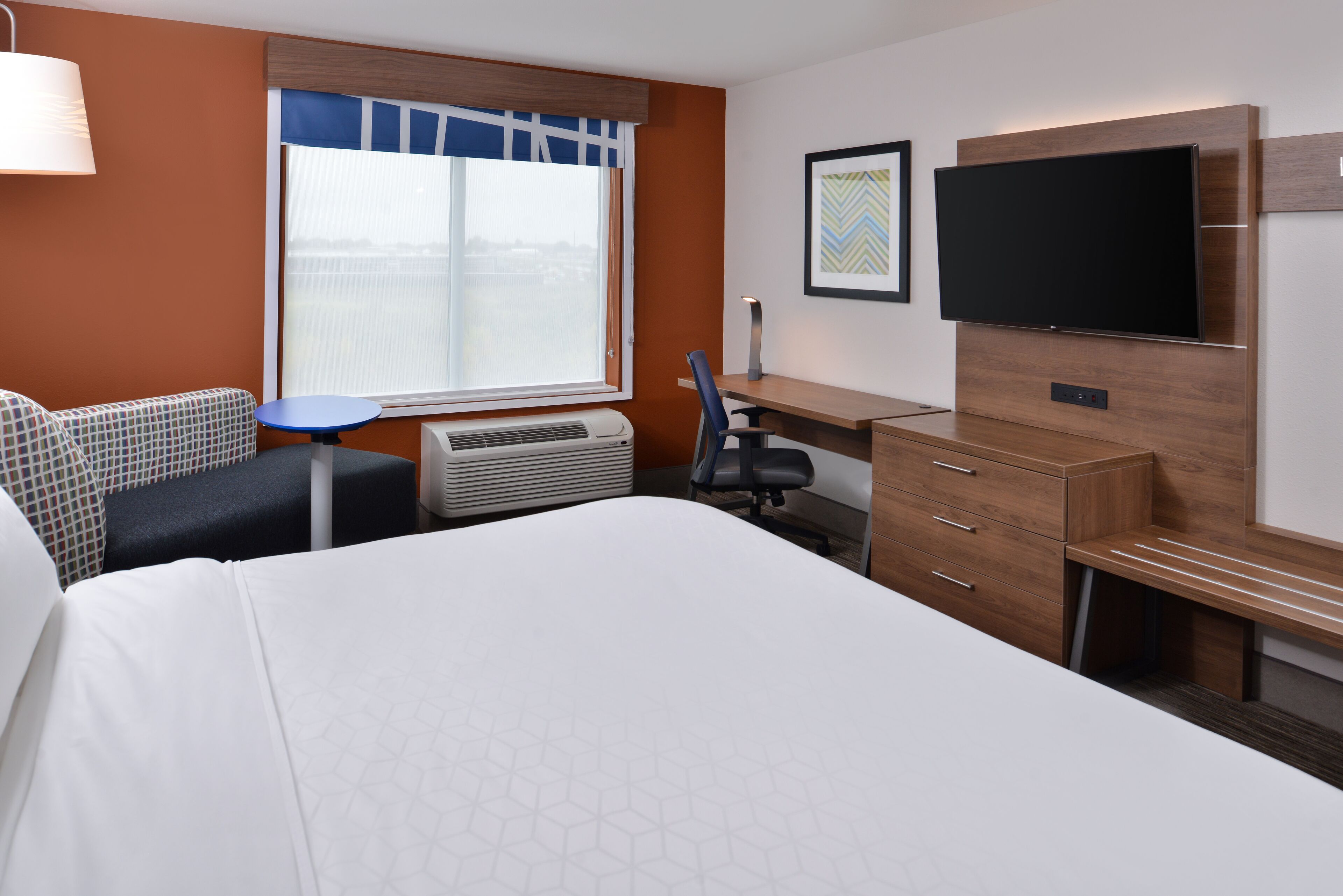 A hotel room with a bed, a desk, a chair, a TV, and a window with a view.