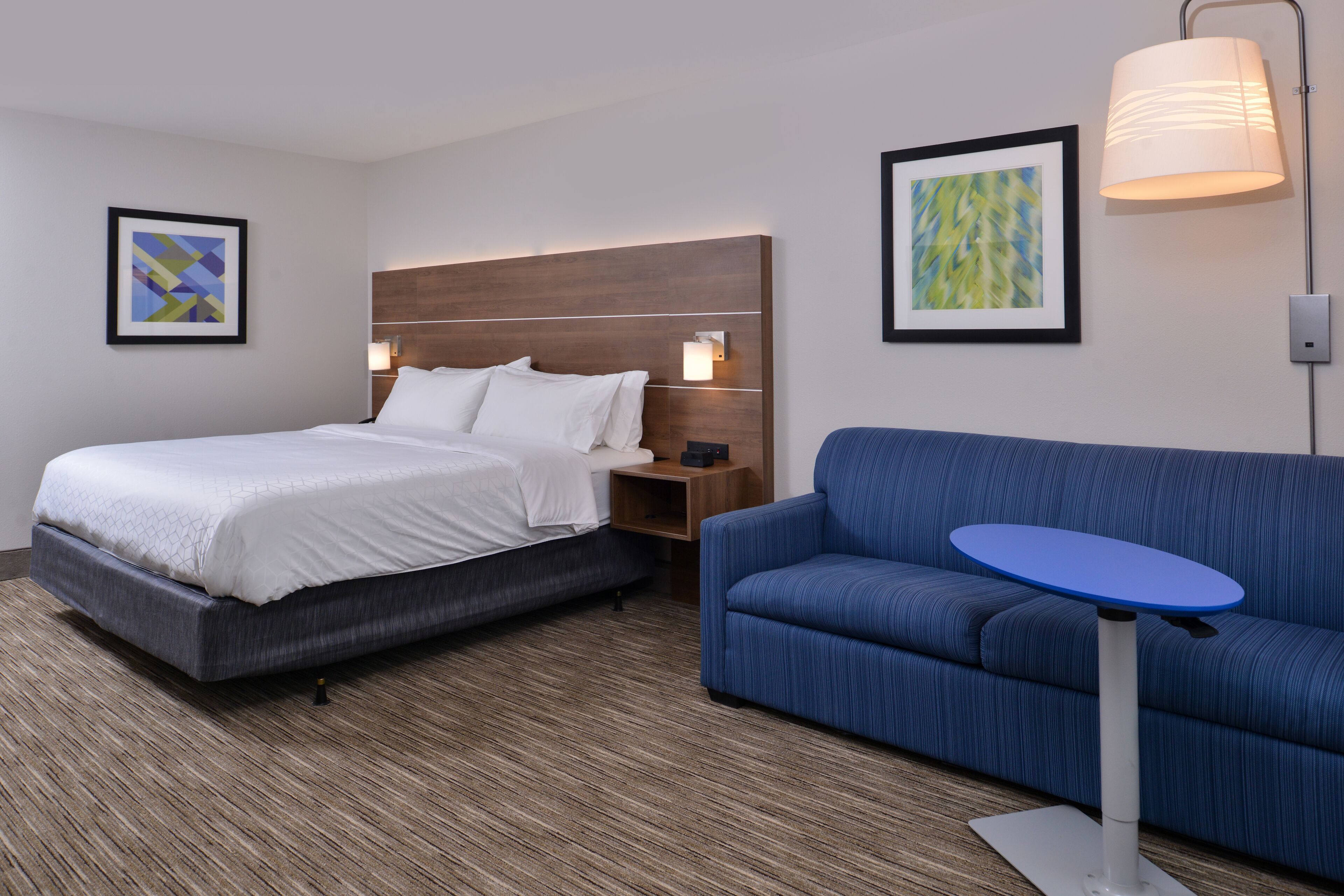 Une chambre d’hôtel avec un lit, un canapé bleu, une petite table et deux lampes fixées au mur.