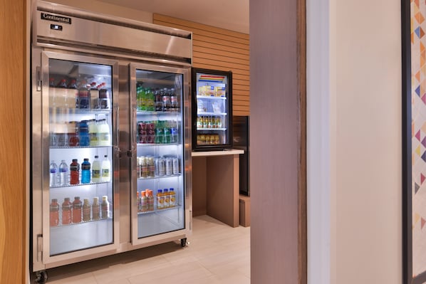 Mostrador refrigerado con diversas bebidas y un reloj digital.