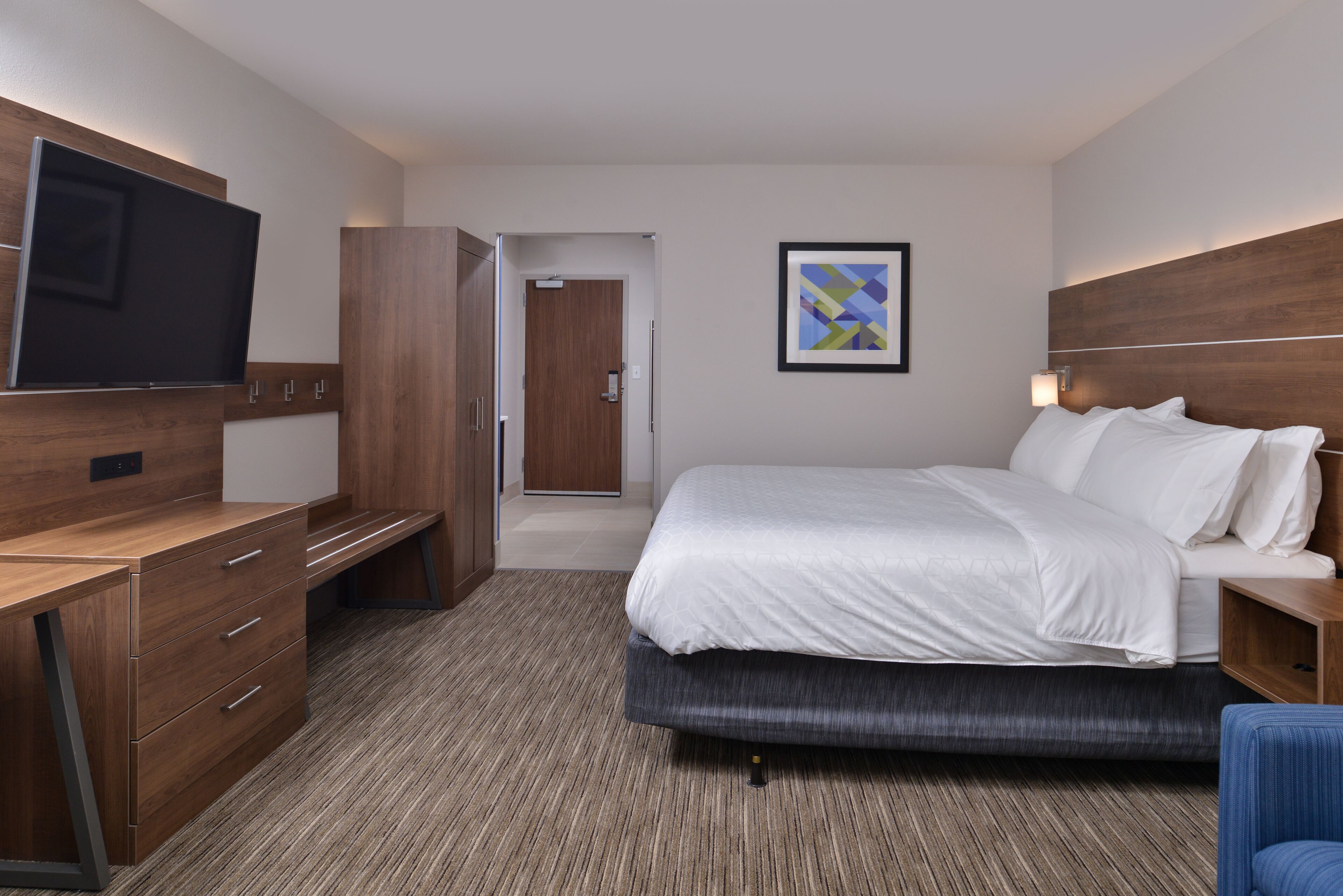 Een hotelkamer met een bed, een bureau, een televisie, een deur en een lijst met een afbeelding aan de muur.