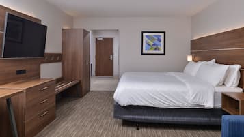 Een hotelkamer met een bed, een bureau, een televisie, een deur en een lijst met een afbeelding aan de muur.