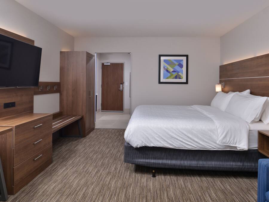 Een hotelkamer met een bed, een bureau, een televisie, een deur en een lijst met een afbeelding aan de muur.