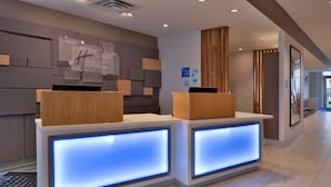 A reception desk with illuminated panels, a wooden reception desk, and a wall-mounted clock. - Holiday Inn Express & Suites Marshalltown by IHG (Marshalltown)