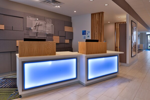 A reception desk with illuminated panels, a wooden reception desk, and a wall-mounted clock. - Holiday Inn Express & Suites Marshalltown by IHG (Marshalltown)