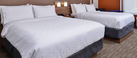 A hotel room with two beds, a wooden headboard, a nightstand, and a wall-mounted lamp.