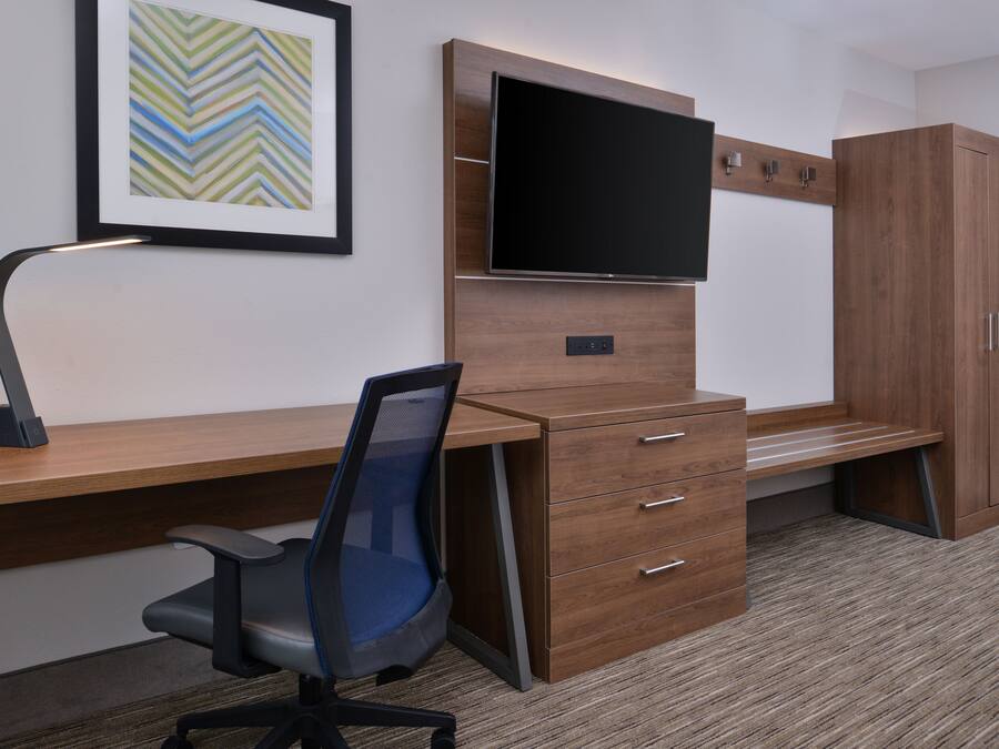 Un espacio de oficina moderno con un escritorio de madera, una silla, un televisor de pantalla plana montado en un panel de madera y un gabinete grande.