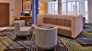 A hotel lobby with a sofa, two armchairs, a small table, and a laptop on a desk. - Holiday Inn Express & Suites Marshalltown by IHG (Marshalltown)