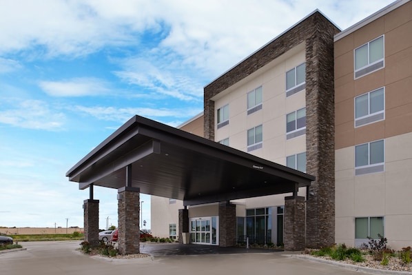 A modern hotel entrance with a covered walkway, stone pillars, and a parking lot. - Holiday Inn Express & Suites Marshalltown by IHG (Marshalltown)