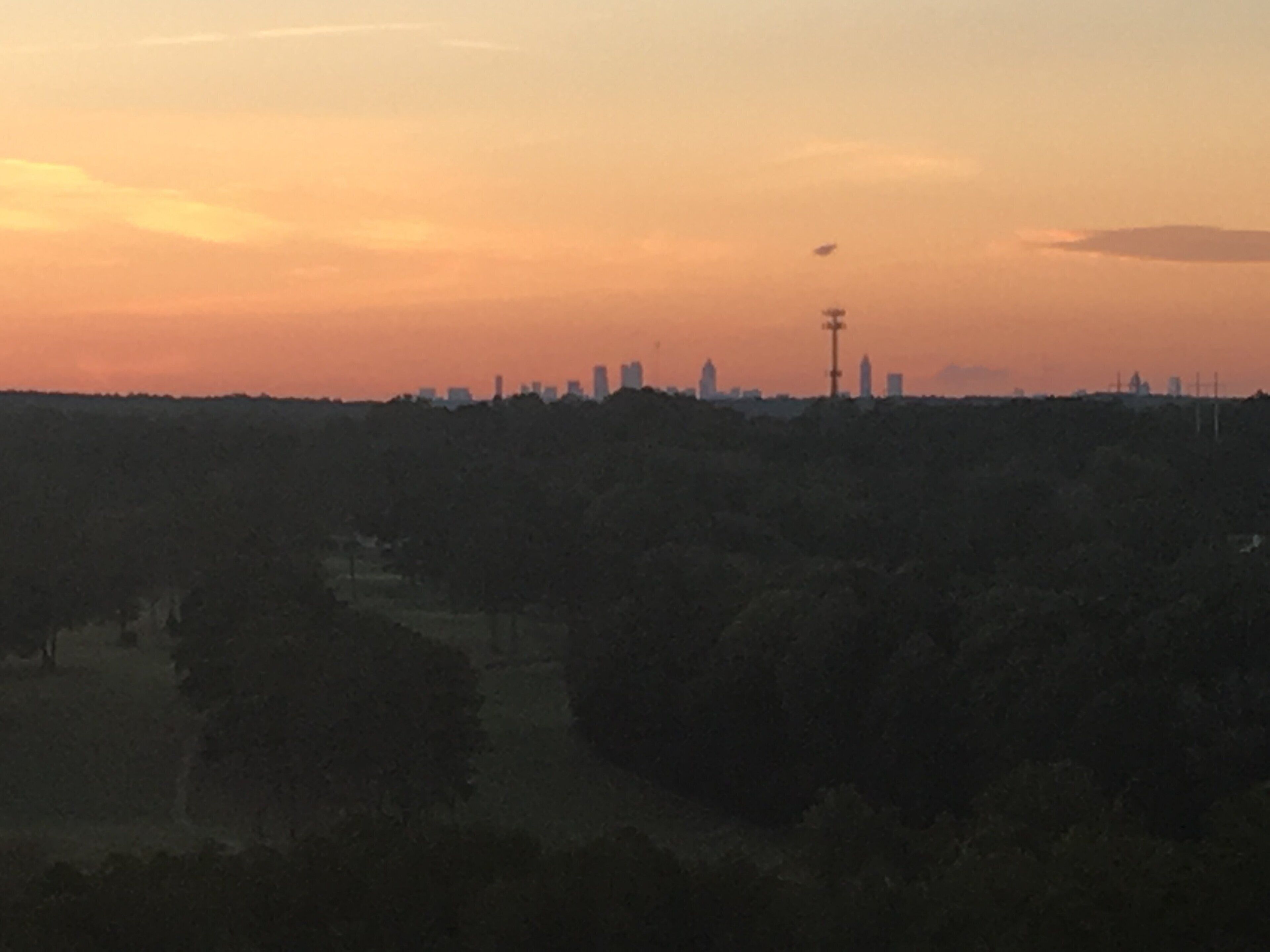A city skyline at dusk with silhouettes of buildings and a distant tower.