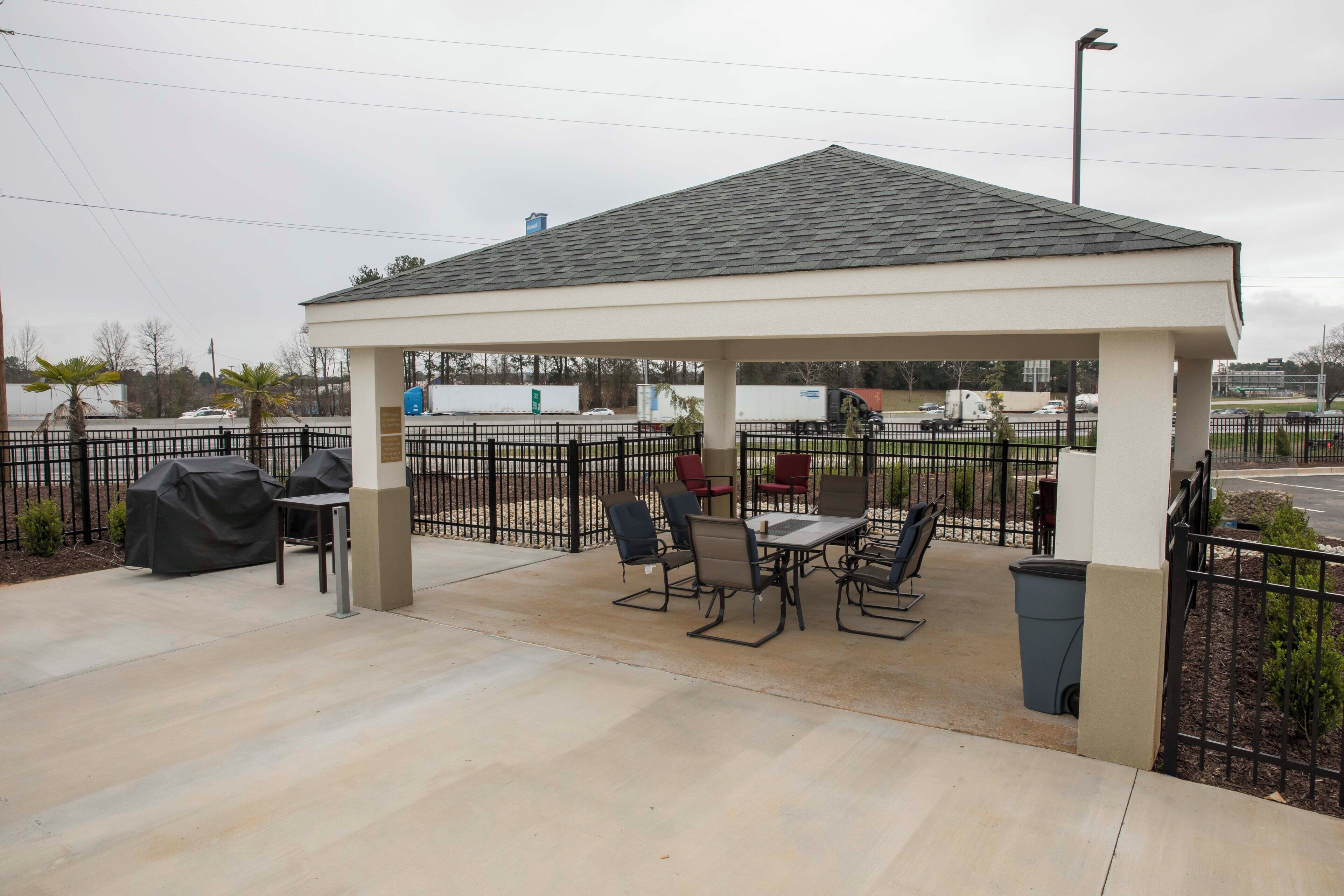 A covered outdoor seating area with tables and chairs, a trash bin, and a grill.
