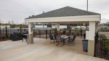 A covered outdoor seating area with tables and chairs, a trash bin, and a grill.