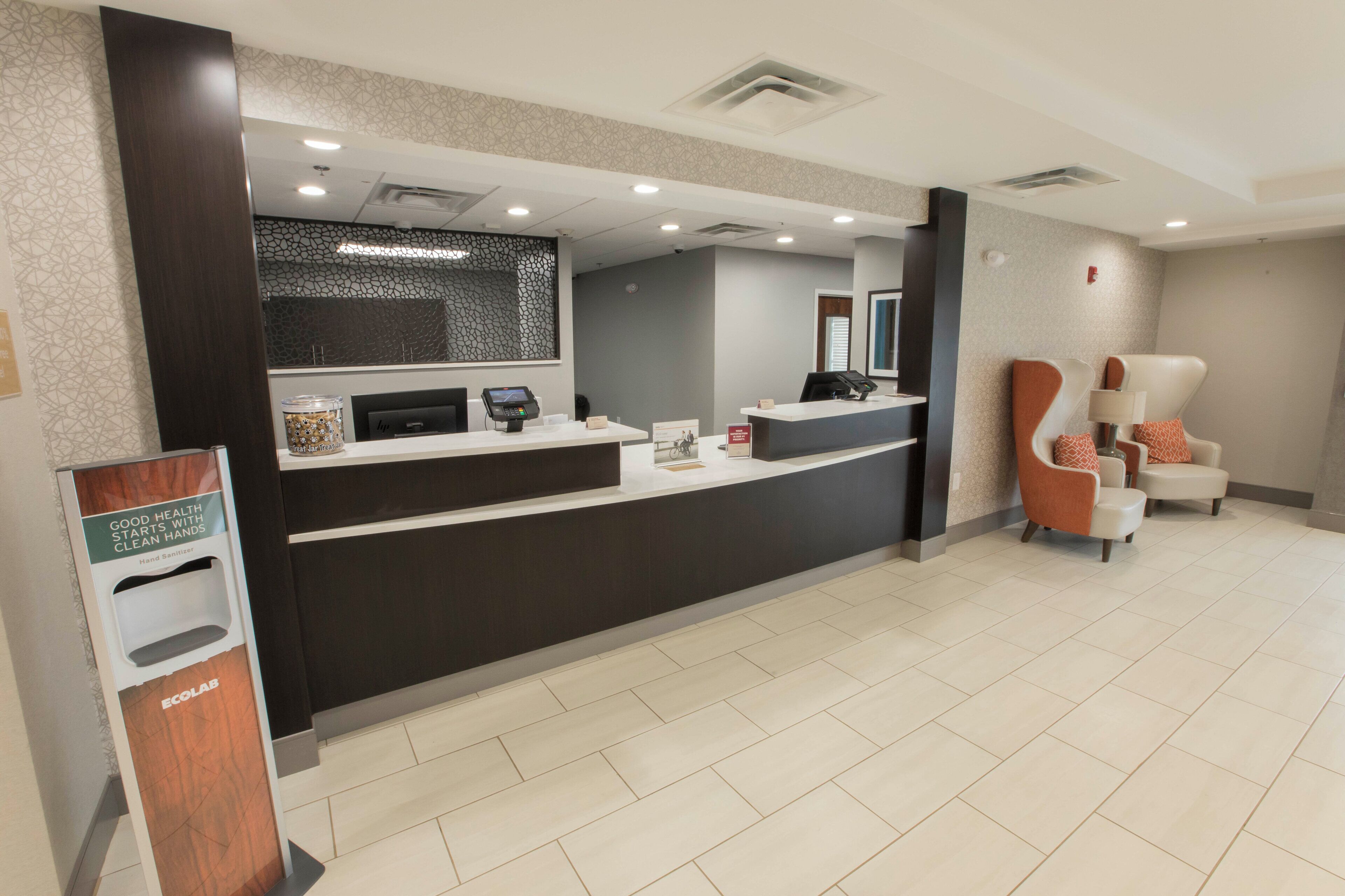 A reception area with a counter, hand sanitizer dispenser, and seating with a modern design.