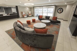 Ein stilvoller Lounge-Bereich mit einem grauen Sofa, zwei runden Tischen und orangefarbenen Hocker.
