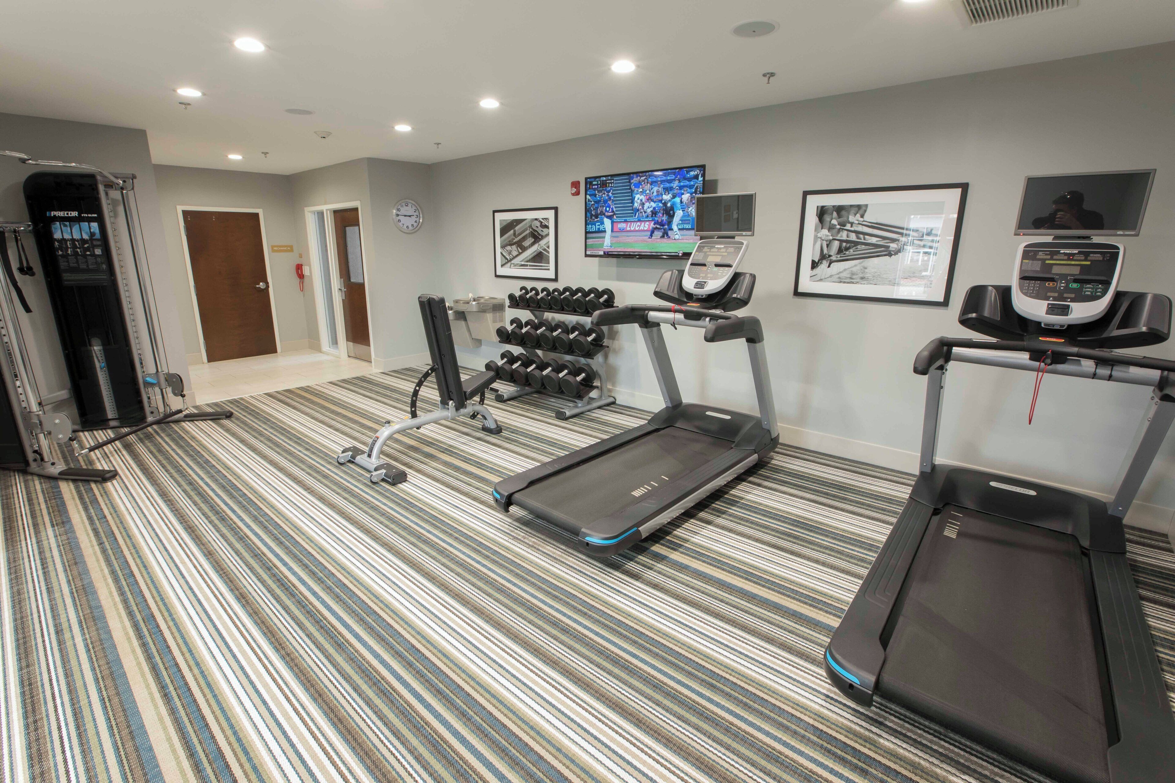 A hotel fitness room with treadmills, dumbbells, and a wall-mounted TV.