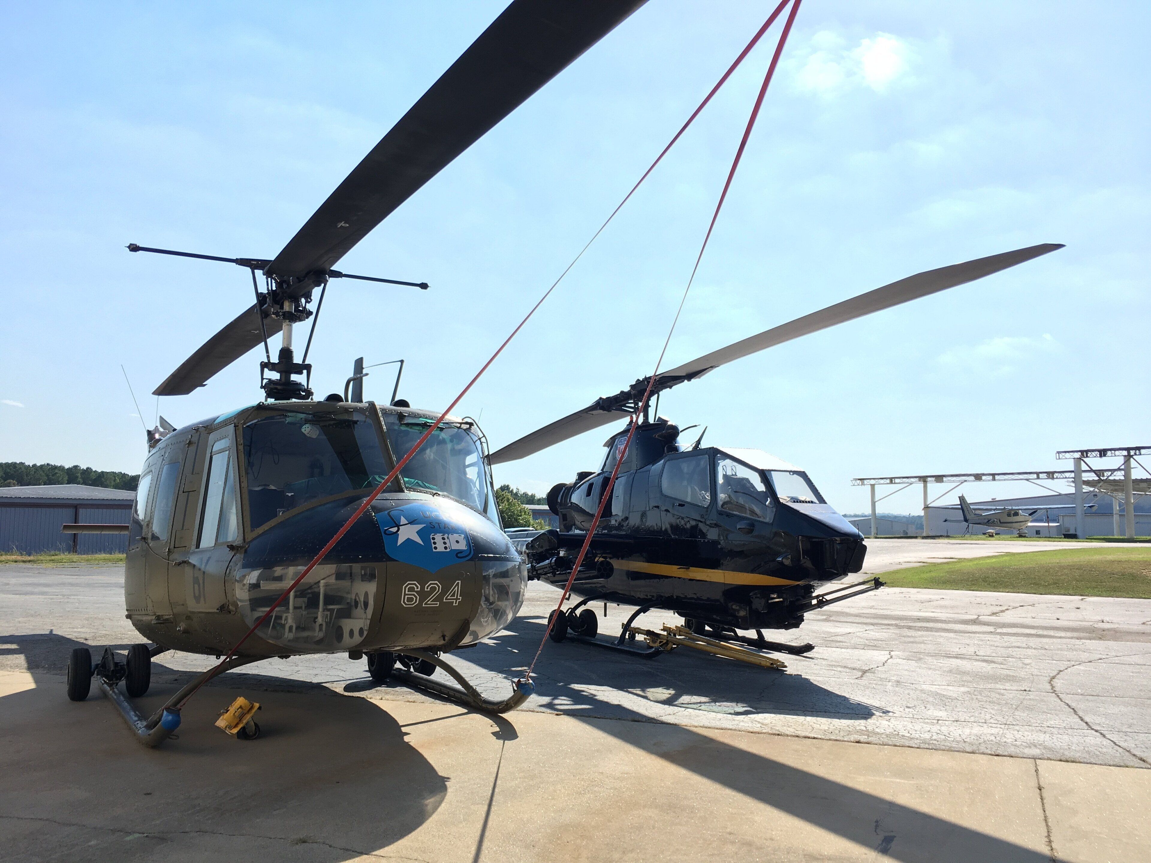 Twee helikopters staan geparkeerd op een betonvlakte, met een heldere lucht op de achtergrond.