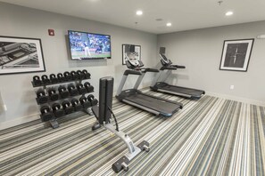 Ein Fitnessstudio mit Laufbändern, Hanteln und einem Fernsehbildschirm.