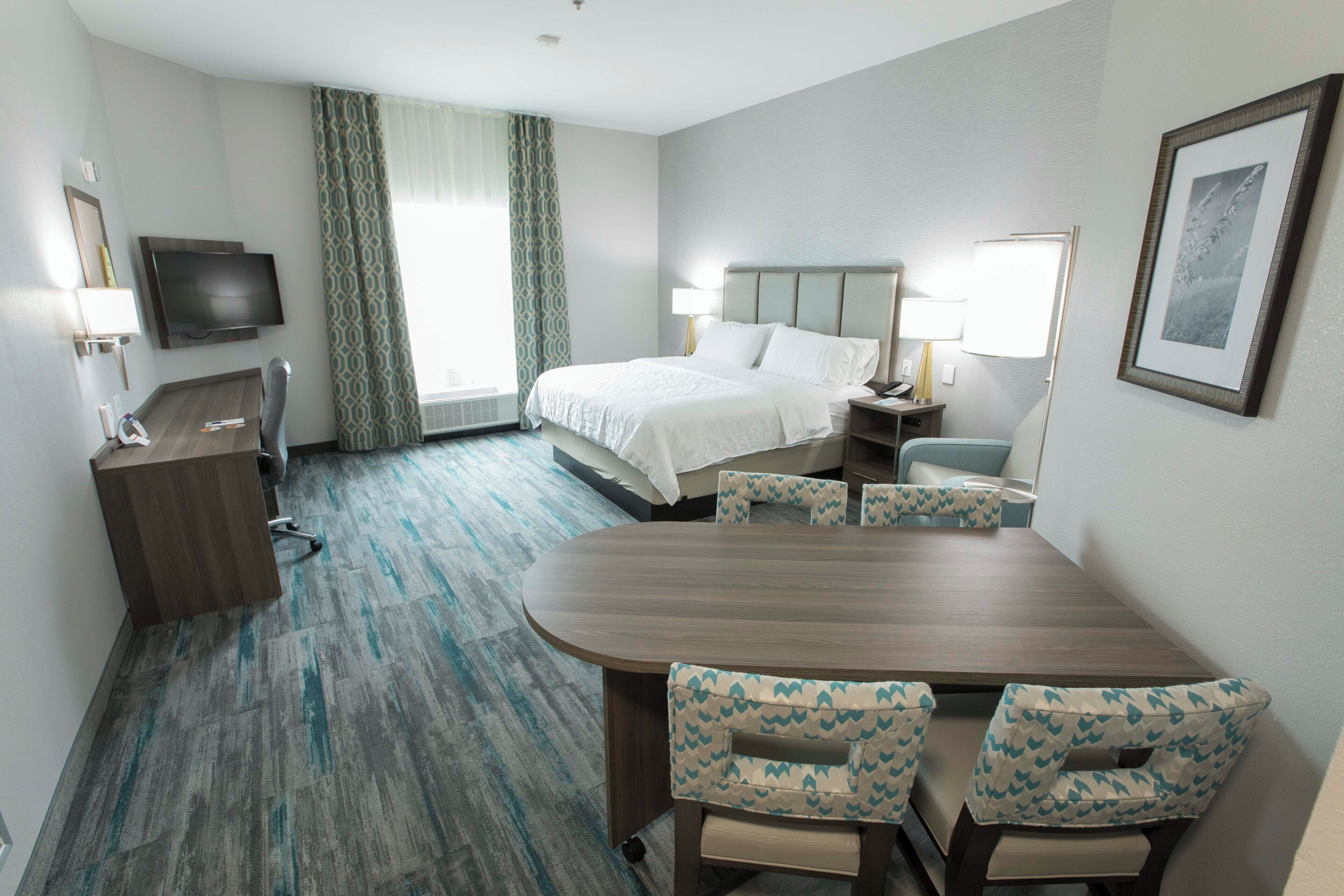 Una habitación de hotel con cama, escritorio, silla, televisión y un rincón de comedor con sillas.