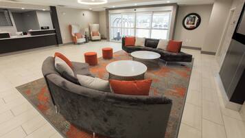 Un espacio lounge moderno con un sofá gris, dos mesas redondas y un mostrador de recepción.