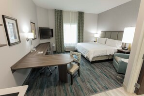 A hotel room with a bed, desk, chair, television, and a window with curtains. - Candlewood Suites McDonough by IHG (McDonough)
