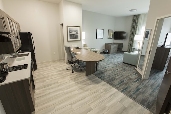 A modern hotel room with a kitchen area, a dining table, and a seating area.