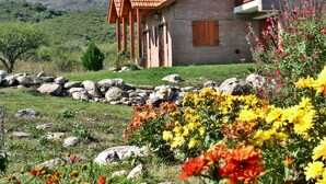 A rustic building with a tiled roof and a balcony, surrounded by a natural landscape with mountains in the background. - Cabañas Oma Lissi (Merlo)