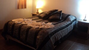 A neatly made bed with a patterned bedspread, a bedside lamp, and a vase on the nightstand. - Cabañas Oma Lissi (Merlo)