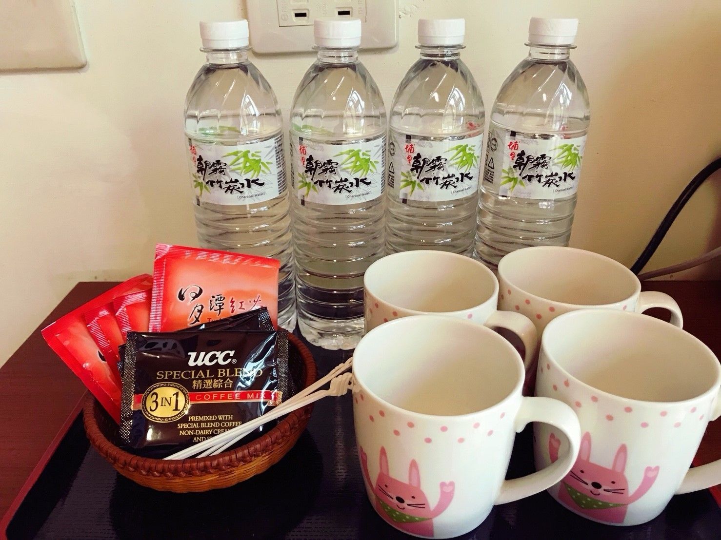 A table with four bottles of water, a packet of coffee mix, and several mugs.