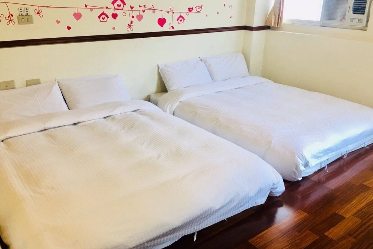 Dos camas individuales con sábanas blancas en una habitación con suelo de madera.