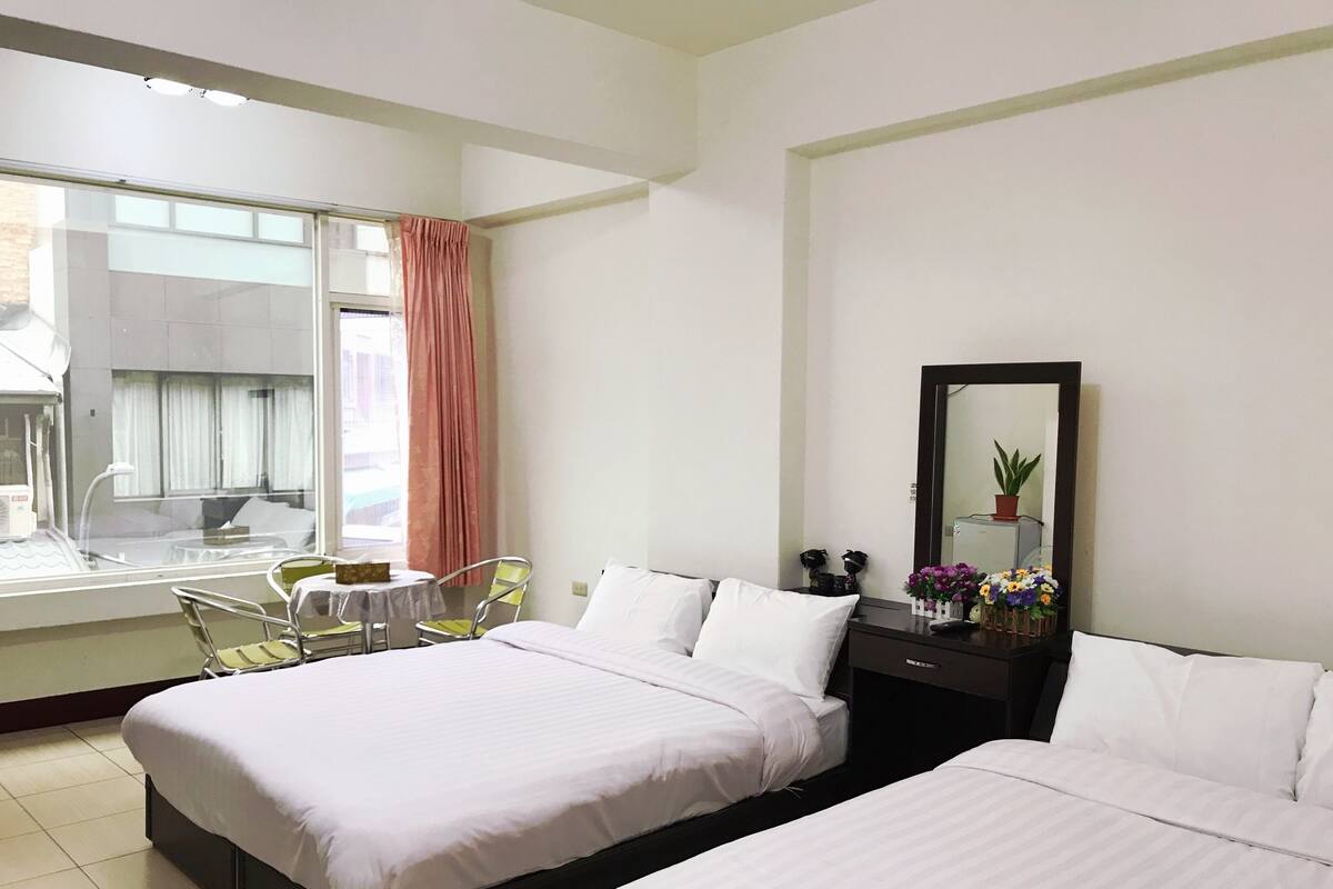 Habitación de hotel con dos camas, un escritorio, una silla, una ventana con cortinas y un espejo.