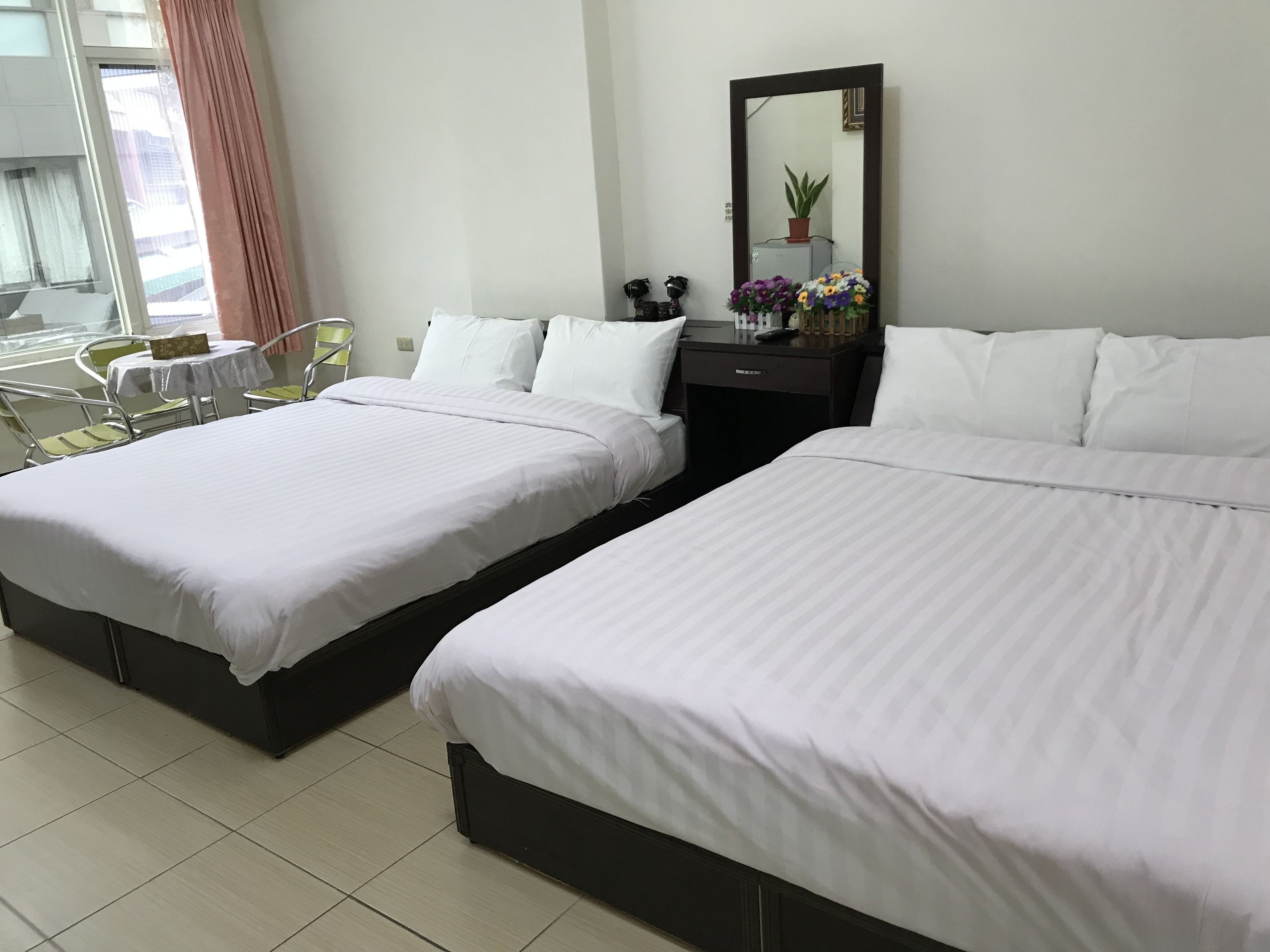Habitación de hotel con dos camas, una mesita con sillas, un escritorio con espejo y una planta en maceta.