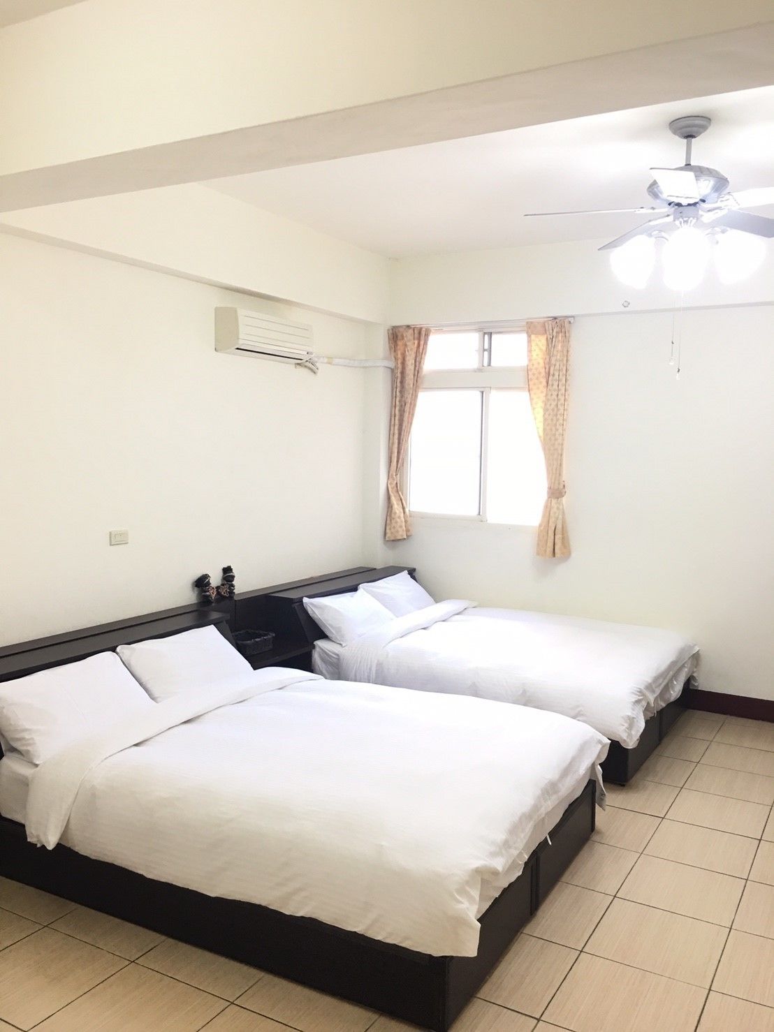 Une chambre d’hôtel avec deux lits, un ventilateur de plafond, un appareil de climatisation et une fenêtre avec des rideaux.